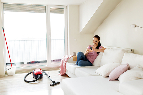 cleaning, household and technology concept - happy woman or housewife with smartphone and vacuum cleaner at home