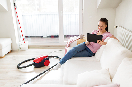 cleaning, household and technology concept - happy woman or housewife with tablet pc computer and vacuum cleaner at home