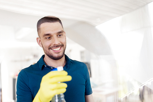 household and people concept - man in rubber gloves cleaning window with spray cleaner at home