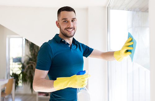 household and people concept - man in rubber gloves cleaning window with rag and spray cleaner at home