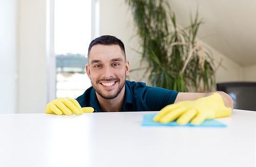 household, cleaning and people concept - smiling man wiping table with cloth at home
