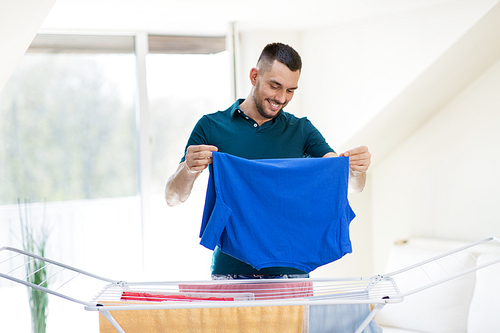 laundry and household concept - happy man taking clothes from drying rack and putting them to basket at home
