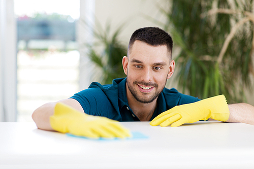 household, cleaning and people concept - smiling man wiping table with cloth at home