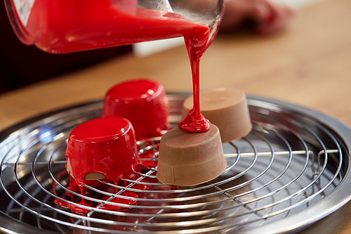 cooking, baking and food concept - jug pouring glaze to chocolate cakes on tray with grid at pastry shop