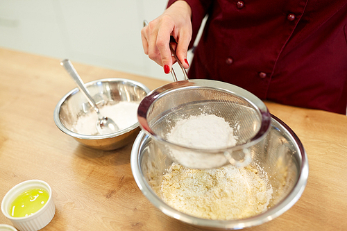 cooking food, baking and people concept - chef with sieve sifting flour into bowl and making batter or dough