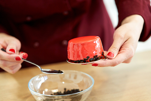 cooking, baking and confectionery concept - chef decorating mirror glaze cakes with chockolate sprinkles at pastry shop