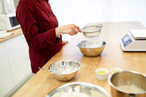 cooking food, baking and people concept - chef with sieve sifting flour into bowl and making batter or dough