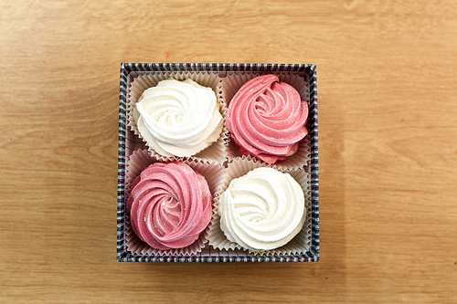 food, confection and sweets concept - zephyr, marshmallow or whipped cream in gift box on wooden table