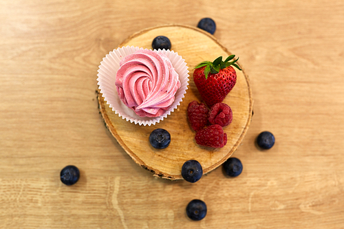 food, confection and sweets concept - zephyr, marshmallow or whipped cream with berries on wooden stand