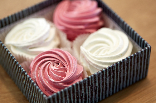 food, confection and sweets concept - close up of zephyr, marshmallow or whipped cream in gift box on wooden table