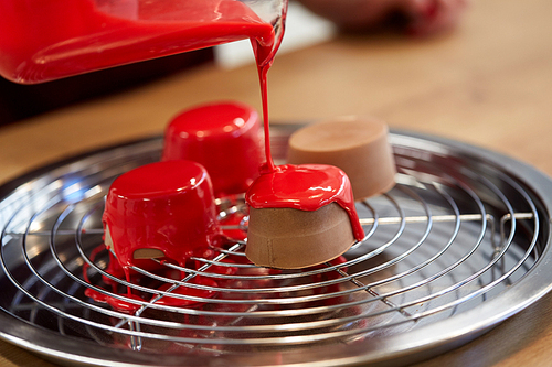 cooking, baking and food concept - jug pouring glaze to chocolate cakes on tray with grid at pastry shop