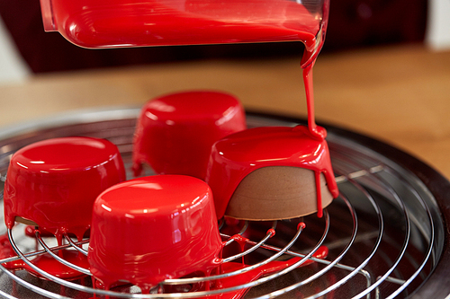 cooking, baking and food concept - jug pouring glaze to chocolate cakes on tray with grid at pastry shop