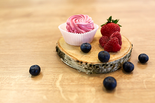 food, confection and sweets concept - zephyr, marshmallow or whipped cream with berries on wooden stand