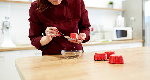 cooking, baking and confectionery concept - chef decorating mirror glaze cakes with chocolate sprinkles at pastry shop