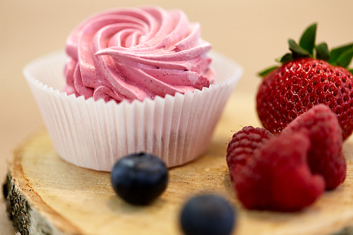 food, confection and sweets concept - zephyr, marshmallow or whipped cream with berries on wooden stand