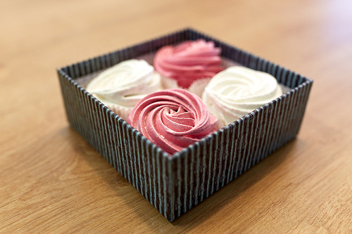 food, confection and sweets concept - zephyr, marshmallow or whipped cream in gift box on wooden table
