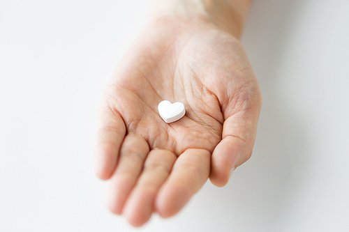 medicine, nutritional supplements and people concept - close up of hand holding pill in shape of heart