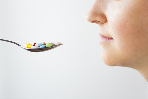 medicine, healthcare and people concept - close up of female face and spoon with pills