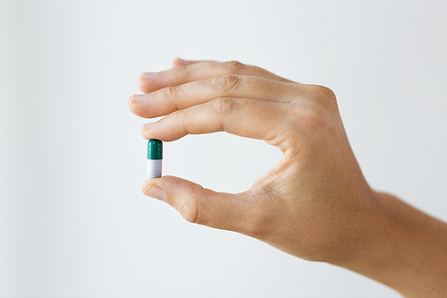 medicine, nutritional supplements and people concept - close up of hand holding capsule of drug