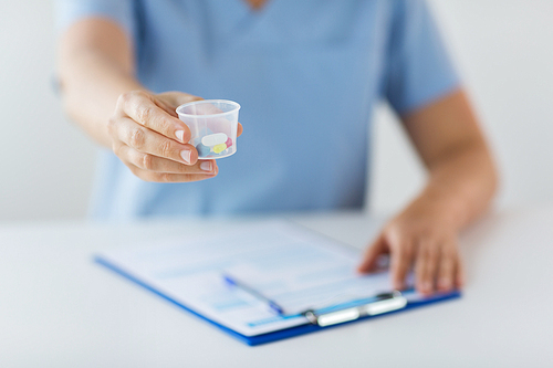 medicine, healthcare and people concept - nurse or doctor with pills in medical cup and clipboard