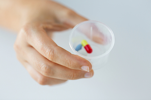 medicine, healthcare and people concept - close up of female hand holding cup with pills