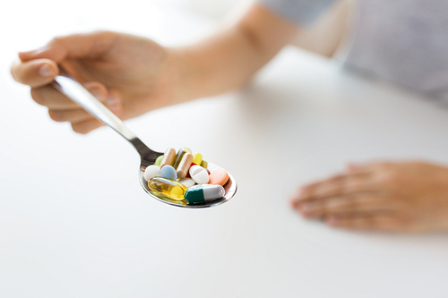medicine, healthcare and people concept - close up of female hand holding spoon with pills