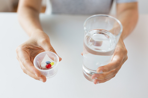 medicine, healthcare and people concept - close up of female hands holding cup with pills and glass of water