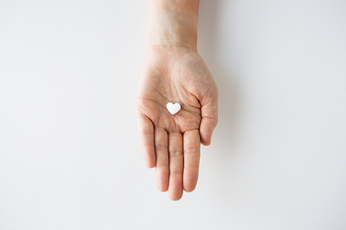 medicine, nutritional supplements and people concept - close up of hand holding pill in shape of heart