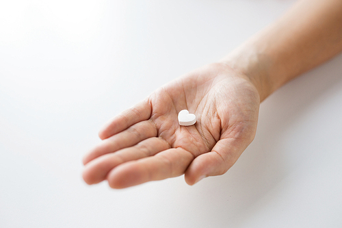 medicine, nutritional supplements and people concept - close up of hand holding pill in shape of heart