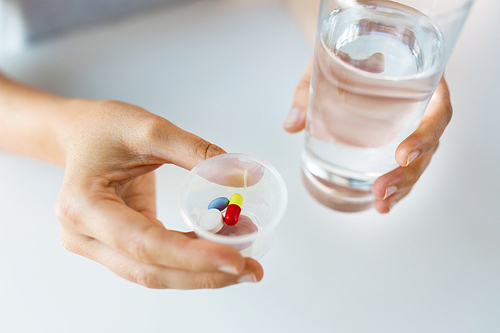 medicine, healthcare and people concept - close up of female hands holding cup with pills and glass of water