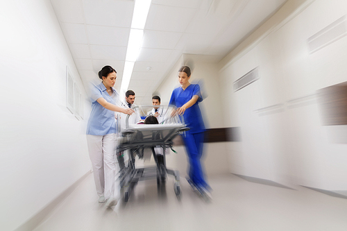 health care, reanimation and medicine concept - group of medics or doctors carrying unconscious woman patient on hospital gurney to emergency (motion blur effect)