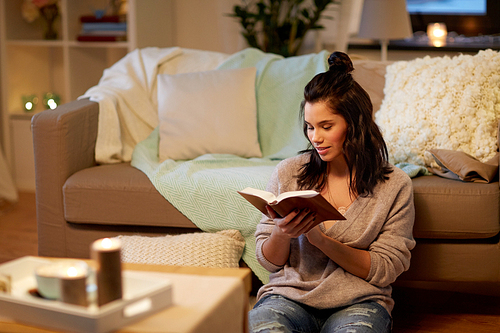 leisure, hygge and people concept - happy young woman reading book at home