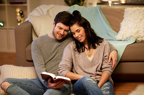 leisure, hygge and people concept - happy couple reading book at home