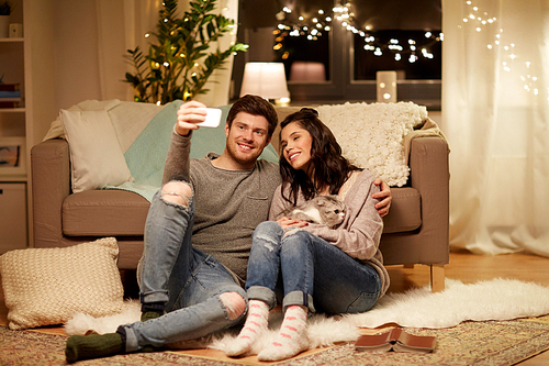 leisure, technology and people concept - happy couple with cat taking selfie by smartphone at home