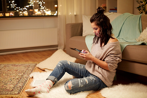 hygge, technology and people concept - happy young woman with smartphone at home