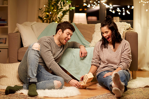 entertainment and people concept - happy couple playing block-stacking game at home