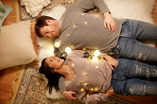 leisure, hygge and people concept - happy couple with garland at home