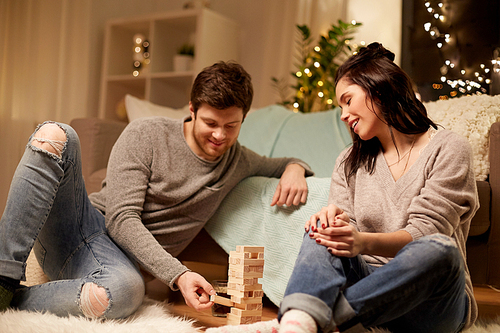 entertainment and people concept - happy couple playing block-stacking game at home