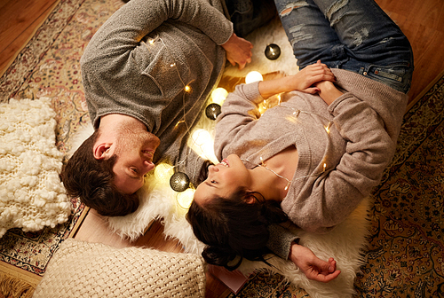 leisure, hygge and people concept - happy couple with garland lying on floor at home