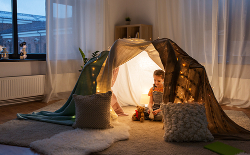 childhood and hygge concept - happy little girl with toys in kids tent at home