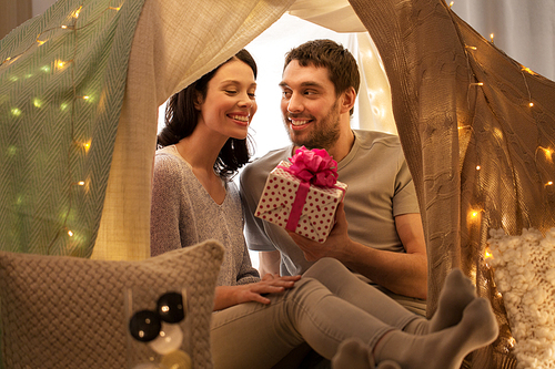 leisure, hygge and people concept - happy couple with gift box in kids tent at home