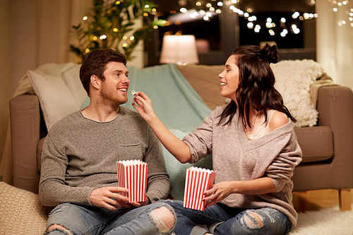 hygge, leisure and people concept - happy couple eating popcorn at home