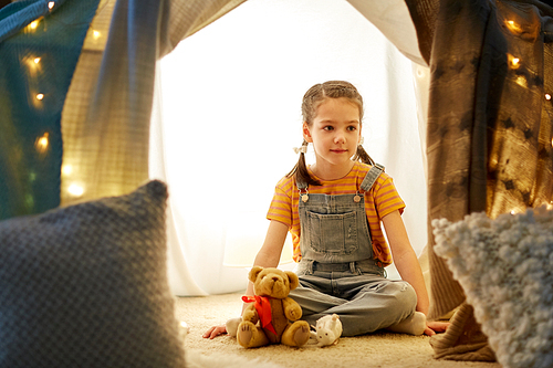 childhood and hygge concept - happy little girl with toys in kids tent at home