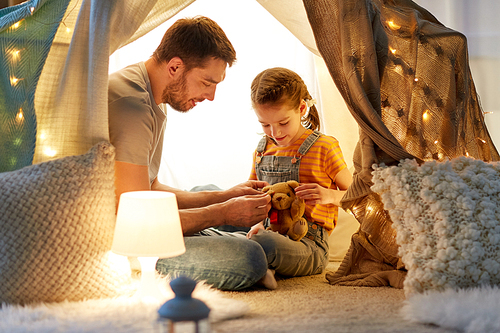 family, hygge and people concept - happy father with teddy bear toy and little daughter playing in kids tent at night at home