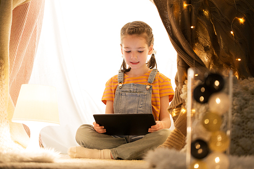 childhood, technology and hygge concept - happy little girl with tablet pc computer in kids tent at home