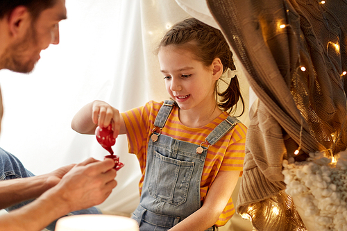 family, hygge and people concept - happy father and little daughter playing tea party in kids tent at night at home