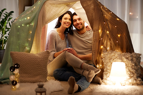 leisure, hygge and people concept - happy couple in kids tent at home