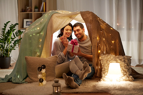 leisure, hygge and people concept - happy couple with gift box in kids tent at home