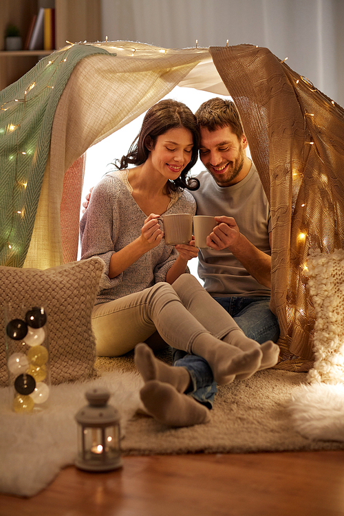 leisure, hygge and people concept - happy couple drinking coffee or tea in kids tent at home