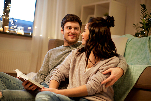 leisure, hygge and people concept - happy couple reading book at home